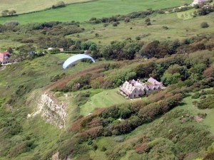 Photo of a paraglider flying near a large house atop a coastal cliff