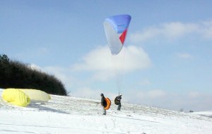 Photo of two paragliders preparing to launch from snowy ground