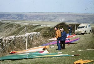 Roly, Peter T, and Roly's mum with flat-rigged hang gliders behind the stone wall at Kimmeridge in 1979