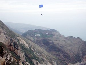 Photo of a paraglider in flight over rugged terrain